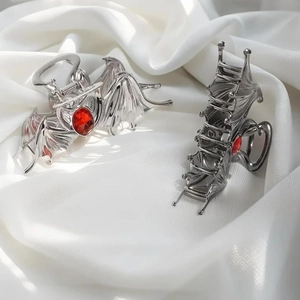 Detailed view of silver bat wing hair claws with a red gemstone on white silk