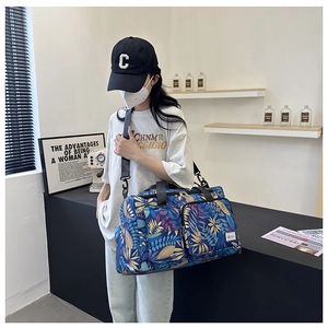 Blue travel tote bag with colorful leaf patterns featuring front zipper pockets and strap