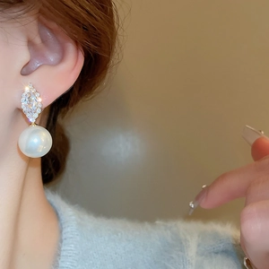Detail of elegant gold earrings with marquise zircon and a large white pearl drop