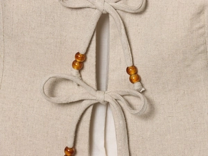 Close-up of beige linen vest featuring drawstring closure with amber beaded details