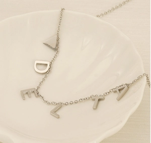 Collier en acier titane argenté avec lettres DELTA posé sur un plateau en céramique