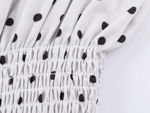 Detailed close-up of white fabric with black polka dots and smocked elastic texture