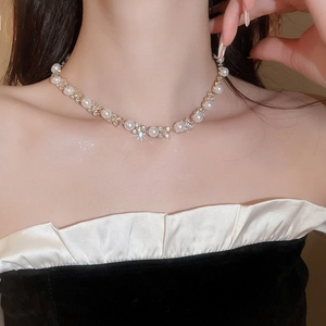 Dettaglio di una collana dorata con perle e strass sulla clavicola di una modella