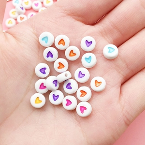 Close-up of round white acrylic beads with colorful heart patterns held in hand