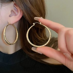 Detail of large gold hoop earrings with hammered texture on a model's ear