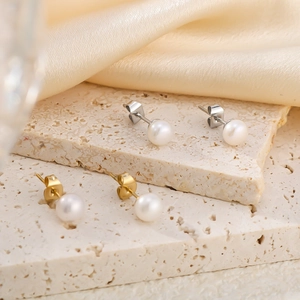 Elegant gold and silver stainless steel pearl earrings set displayed on stone