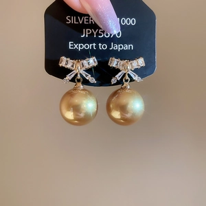 Close-up of sparkling bow knot earrings with large champagne gold pearls on a display card