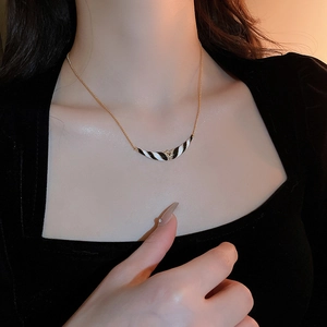 Nahaufnahme einer Goldkette mit schwarz-weiß gestreiftem Emaille-Anhänger an einem Model