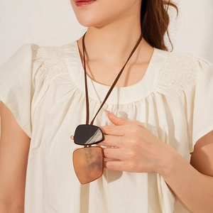 Detail view of irregular square necklace with amber and black pendant on brown cord