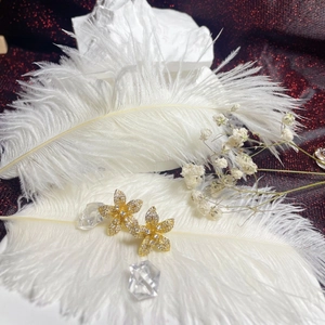 Detailed view of gold flower earrings with pavé crystals on white feathers background