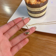 Détail d'un collier doré avec pendentif haricot tenu à la main sur une scène de thé