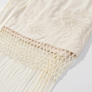 Vue détaillée de la broderie florale et des franges tressées sur tissu crème