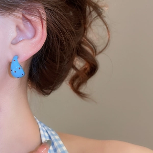 Detail of blue C-shaped earring with red polka dots worn by a model in a close-up view