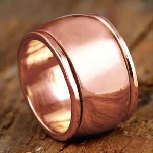 Macro view of polished wide copper ring with engraved edge lines on a wood background
