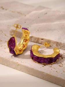 Macro detail of gold-plated C-shape earrings with inlaid purple crystal stones