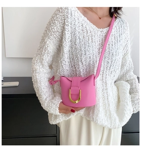 Pink small crossbody bag with gold U-shaped hardware shown worn with a white sweater
