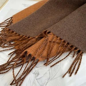 Detail view of double-sided knit scarf with long fringes in brown and caramel tones