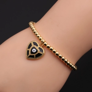 Detail view of a gold-plated beaded bracelet with a heart-shaped evil eye charm on a wrist