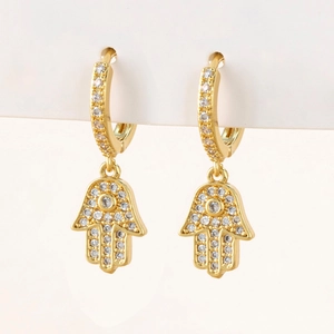 Close-up of gold Hamsa Hand earrings with micro-pave cubic zirconia on white stand