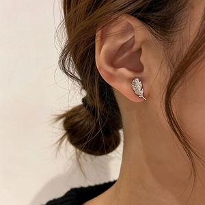 Detailed view of silver leaf stud earrings with pavé crystals on a female model