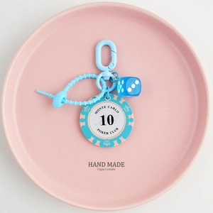 Detail of blue Monte Carlo poker chip and dice keychain on a pink pastel tray
