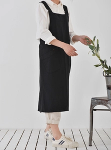 Side view of a black long linen apron with pockets worn by a model in a minimalist setting
