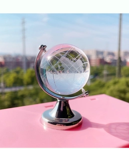 Close-up of a clear crystal globe on a silver metal stand against a pink desk surface