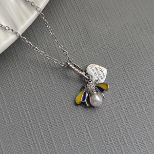 Macro detail of bee pendant with enamel wings, pearl, and engraved small insects heart tag