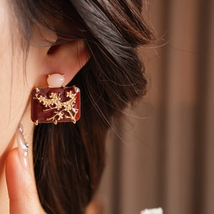 Detail of vintage enamel earring with golden flower pattern and pink gemstone on model