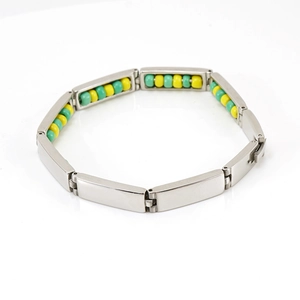 Macro detail of stainless steel bracelet with green and yellow beaded segments on white background