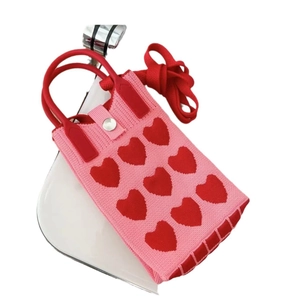 Detail of pink knitted phone bag with red hearts, shoulder strap and silver button