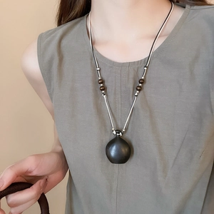 Detail of vintage wooden bead necklace with a black matte kettle pendant on a model