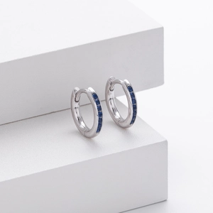 Detailed view of silver hoop earrings featuring blue zircon stones on white stairs