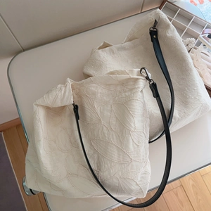 Beige floral embroidered cotton tote bags with black leather straps on a chair