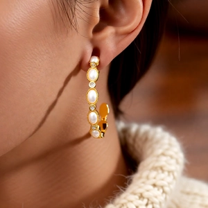 Detail view of gold-plated C-shaped earrings with pearls on a model wearing a sweater