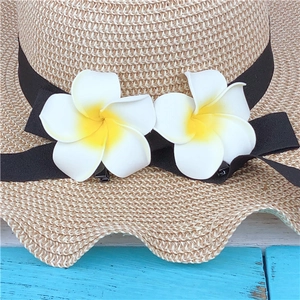 Close-up of a woven straw sun hat with black ribbon and yellow plumeria flower clips