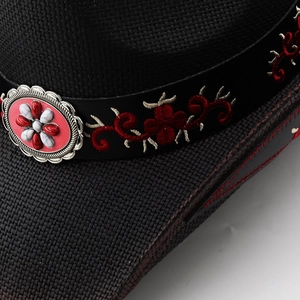 Macro detail of black woven cowboy hat with red floral embroidery and silver bohemian buckle