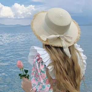 Detail of raffia sun hat with raw fringe edges and ribbon bow against a sea background