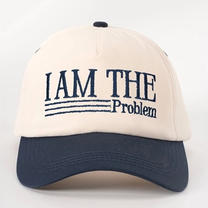 Close-up of I AM THE Problem embroidery on a beige and navy blue cotton baseball cap