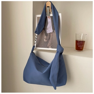 Detail of greyish-blue crossbody bag with knot decor and silver chain on a wall hook