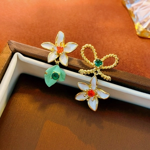 Asymmetric floral bow earrings with colorful enamel and crystals on a jewelry box