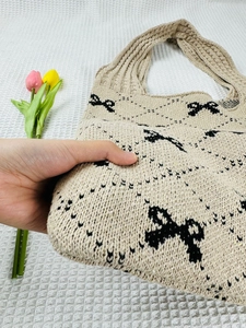 Close-up of soft beige knit tote bag featuring a black bow pattern and textured yarn
