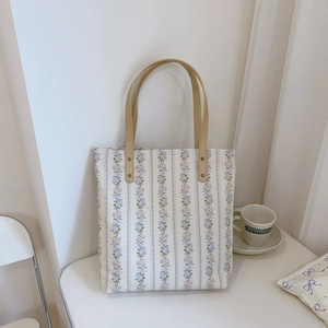 Detail of floral canvas tote bag with purple flower patterns and brown leather handles
