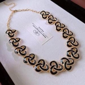 Detail of vintage gold necklace with black enamel knot charms on white background