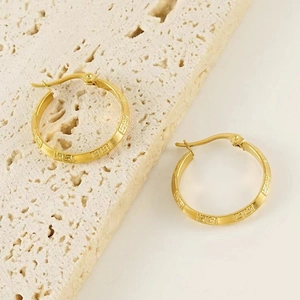 Macro detail of gold-plated stainless steel earrings with Greek key patterns on stone