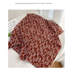 Detail of red-brown floral cotton scarf with white leaf patterns and piping edge on a table