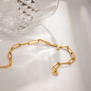 Detailopname van gouden paperclip armband met een kruisbedel op een getextureerde achtergrond