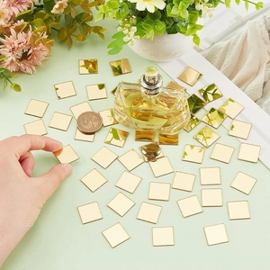 Detail of hand placing small golden square acrylic mirror tiles on a green surface