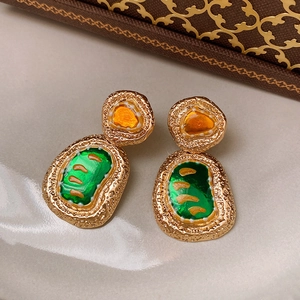 Detailed macro view of vintage baroque gold earrings with green and orange enamel accents