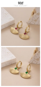 Detail of gold fan-shaped earrings featuring red and green zircons on natural stones